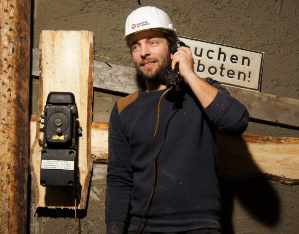 Junger Mann steht im Bergwerk an einem Bergwerkstelefon